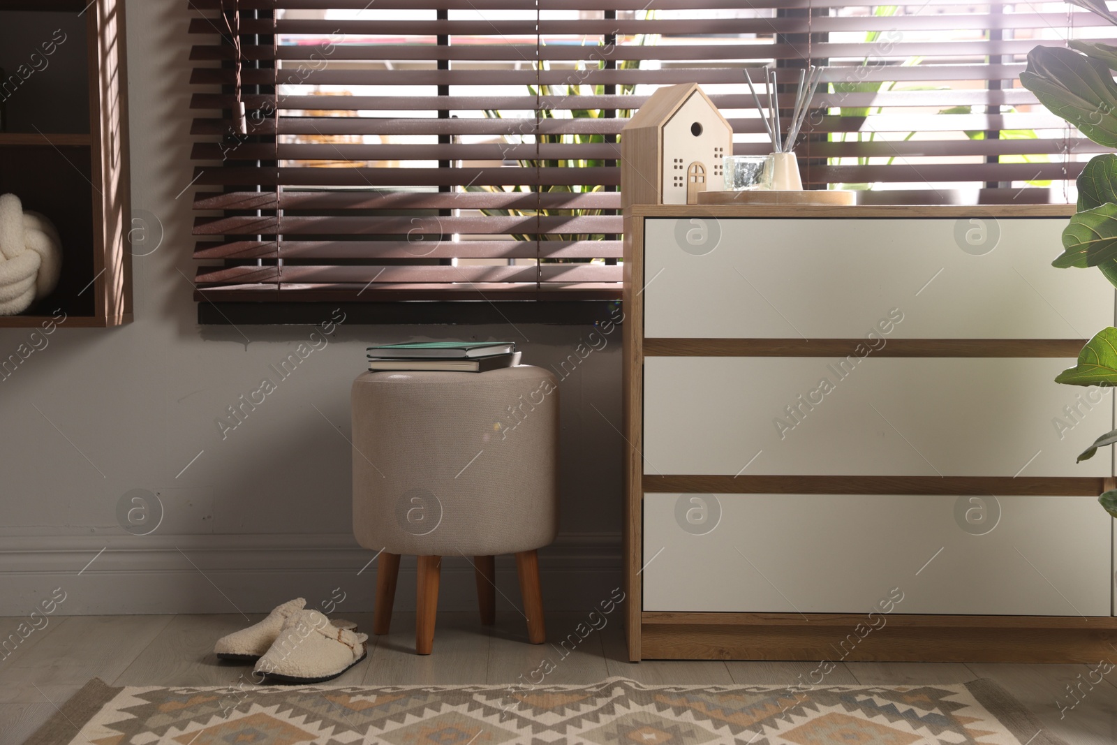 Stylish pouf with books and slippers near chest of drawers at home Photo of Stylish pouf with books and slippers near chest of drawers at home