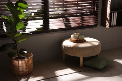 Photo of Stylish pouf with tea set in living room