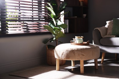 Photo of Stylish pouf with tea set in living room
