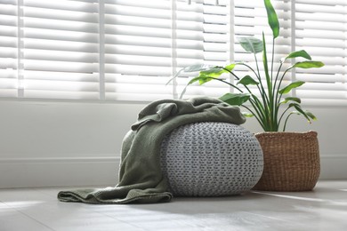 Photo of Stylish knitted pouf with plaid and houseplant at home. Space for text
