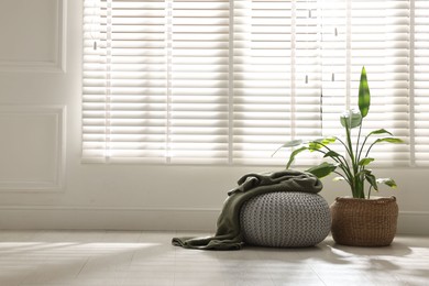 Photo of Stylish knitted pouf with plaid and houseplant at home. Space for text