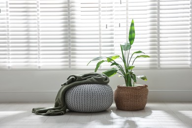 Photo of Stylish knitted pouf with plaid and houseplant at home. Space for text