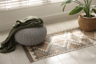 Photo of Stylish knitted pouf with plaid and houseplant at home