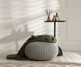 Photo of Stylish knitted pouf with plaid and home decor indoors