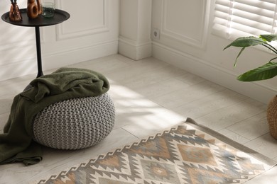 Photo of Stylish knitted pouf with plaid and home decor indoors. Space for text