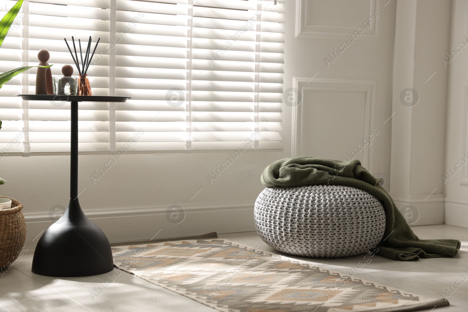 Photo of Stylish knitted pouf with plaid and home decor indoors. Space for text