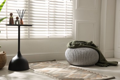 Photo of Stylish knitted pouf with plaid and home decor indoors. Space for text