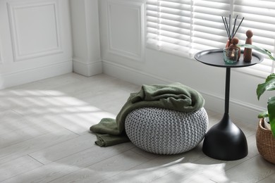 Photo of Stylish knitted pouf with plaid and home decor indoors. Space for text
