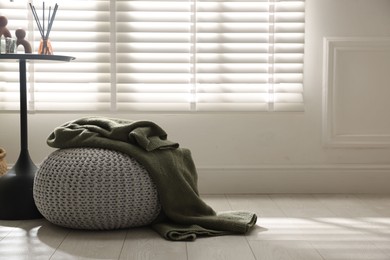 Photo of Stylish knitted pouf with plaid and home decor indoors. Space for text