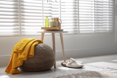 Photo of Stylish knitted pouf with sweater at home. Space for text