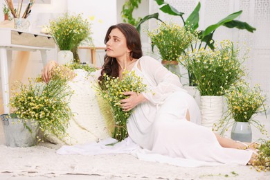 Photo of Beautiful woman with chamomile flowers on floor indoors
