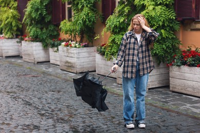 Photo of Frustrated woman with broken umbrella on city street. Space for text