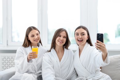 Photo of Happy women in bathrobes taking selfie in spa salon