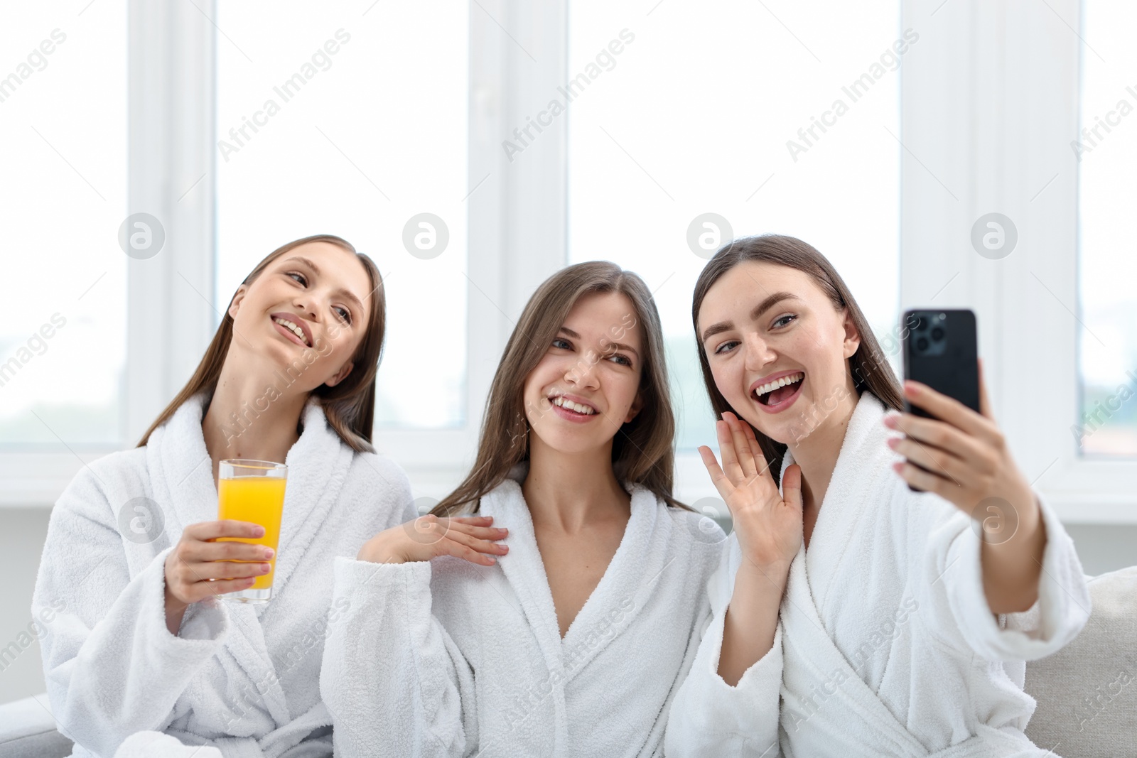 Photo of Happy women in bathrobes taking selfie in spa salon