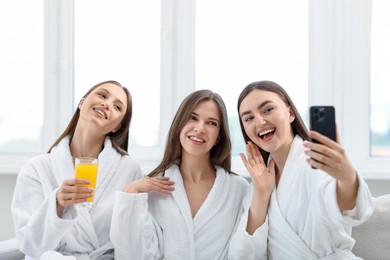 Photo of Happy women in bathrobes taking selfie in spa salon