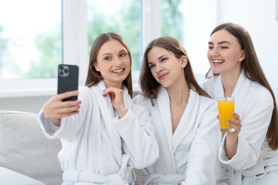 Photo of Happy women in bathrobes taking selfie in spa salon