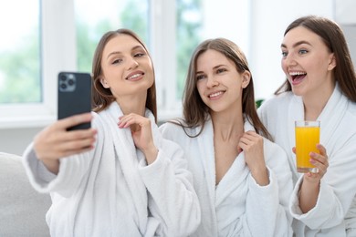 Photo of Happy women in bathrobes taking selfie in spa salon