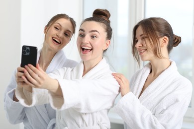 Photo of Happy women in bathrobes taking selfie after spa procedures indoors