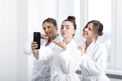 Photo of Happy women in bathrobes taking selfie after spa procedures indoors