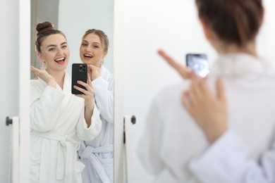 Photo of Happy women in bathrobes taking selfie near mirror after spa procedures indoors