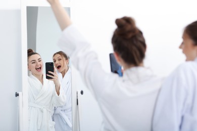 Photo of Happy women in bathrobes taking selfie near mirror after spa procedures indoors