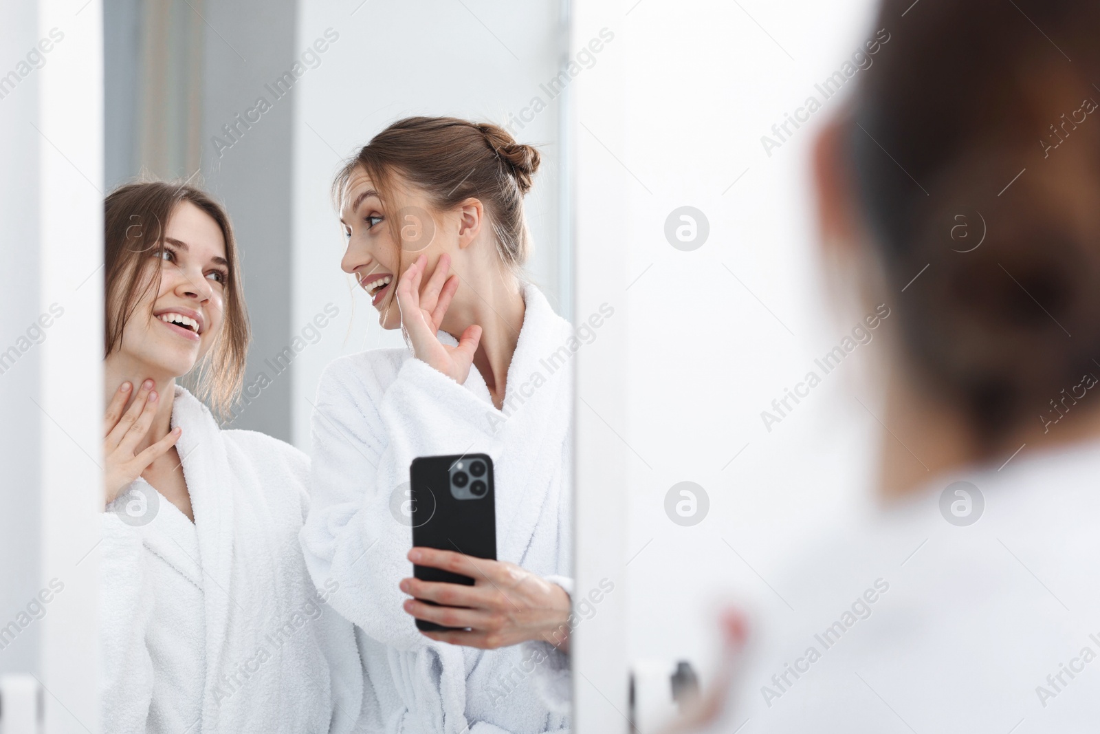 Photo of Happy women in bathrobes taking selfie near mirror after spa procedures indoors