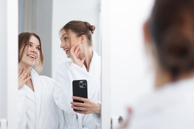 Photo of Happy women in bathrobes taking selfie near mirror after spa procedures indoors