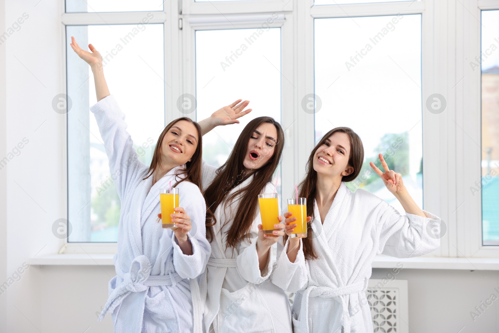 Photo of Happy women in bathrobes with glasses of orange juice after spa procedures indoors