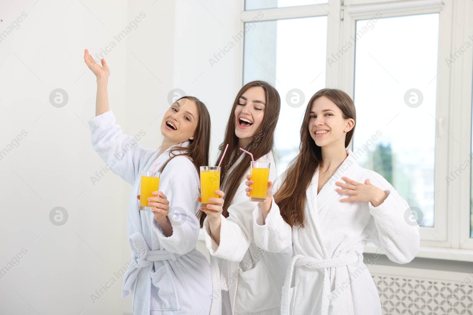 Photo of Happy women in bathrobes with glasses of orange juice after spa procedures indoors