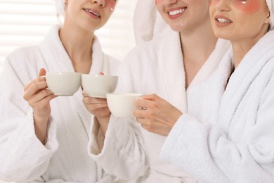 Photo of Happy women in bathrobes with cups of healthy drink after spa procedures indoors, closeup