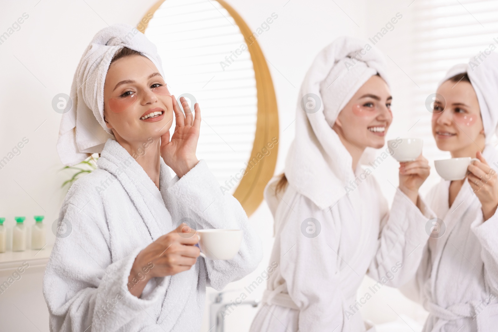 Photo of Happy women in bathrobes with cups of healthy drink after spa procedures indoors, selective focus