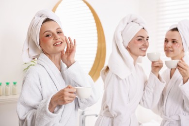 Photo of Happy women in bathrobes with cups of healthy drink after spa procedures indoors, selective focus