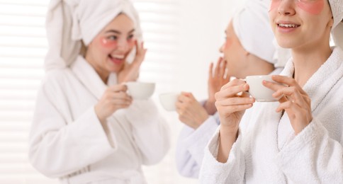Photo of Happy women in bathrobes with cups of healthy drink after spa procedures indoors, selective focus