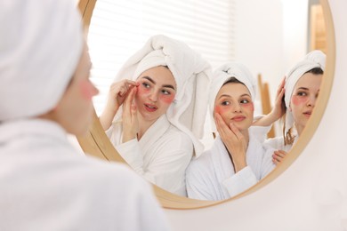 Photo of Happy women in bathrobes applying eye patches after spa procedures near mirror indoors