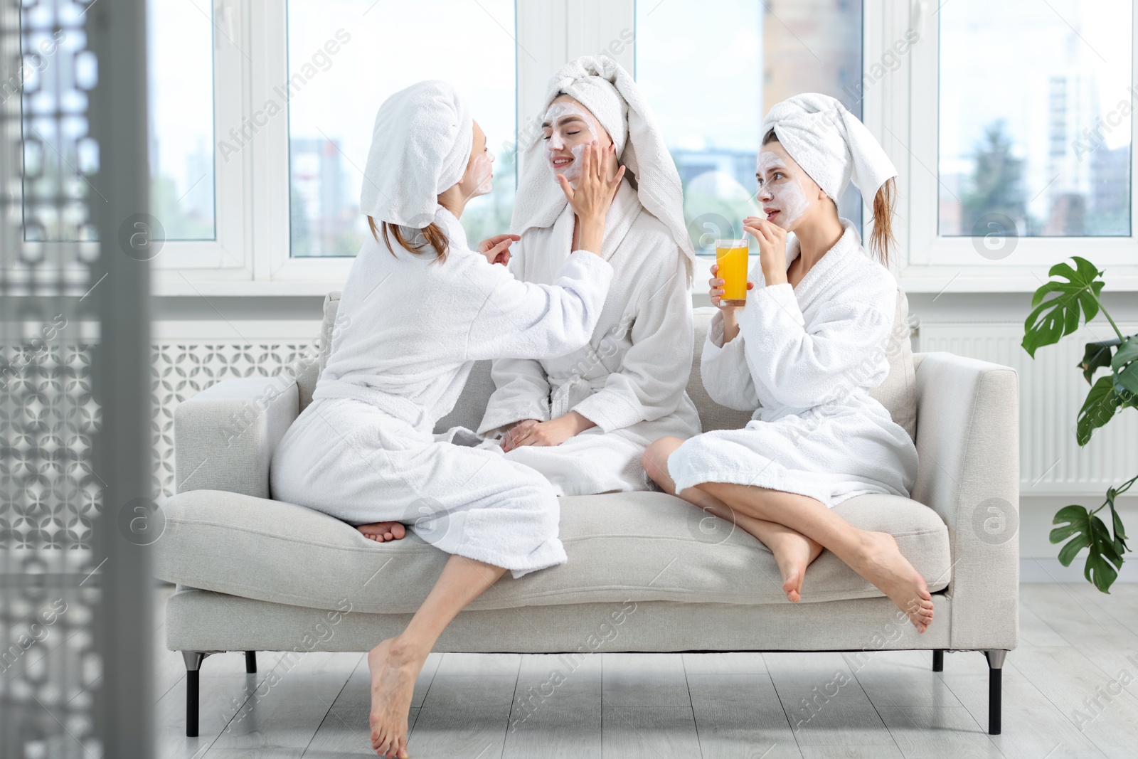 Photo of Happy women in bathrobes spending time together after spa procedures on sofa indoors