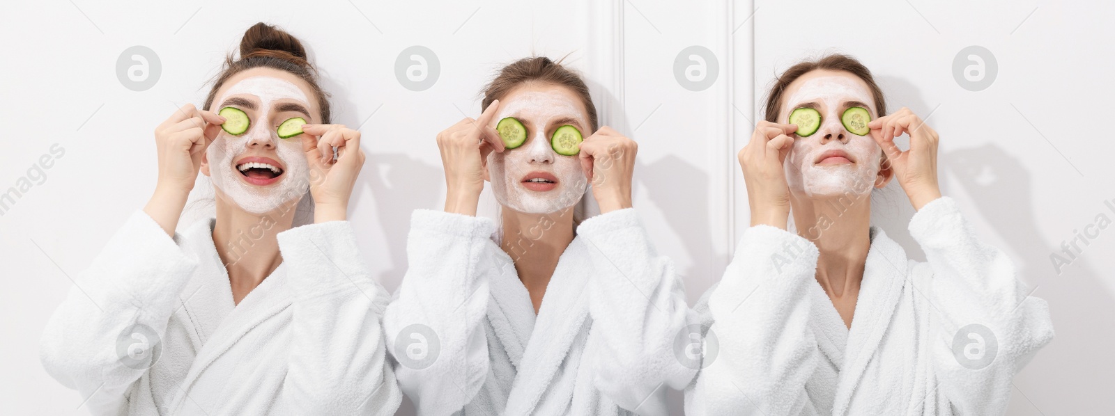 Photo of Happy women with facial masks and cucumber slices in bathrobes after spa procedures near white wall