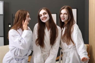 Photo of Happy women with facial masks in bathrobes posing after spa procedures indoors
