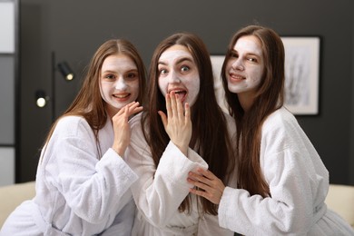 Photo of Happy women with facial masks in bathrobes posing after spa procedures indoors