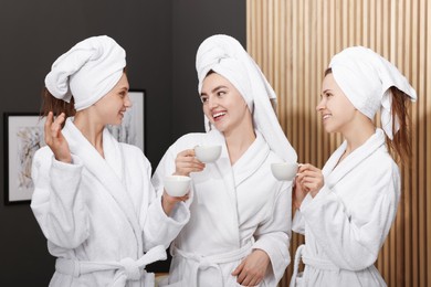 Photo of Happy women with cups of healthy drink in bathrobes after spa procedures indoors