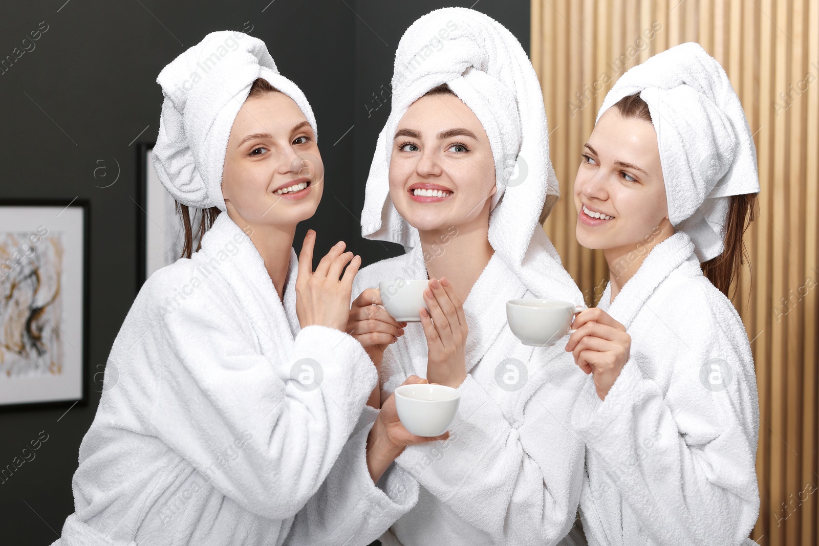 Photo of Happy women with cups of healthy drink in bathrobes after spa procedures indoors