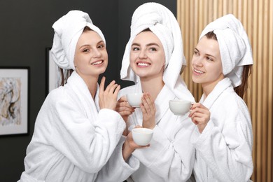 Photo of Happy women with cups of healthy drink in bathrobes after spa procedures indoors