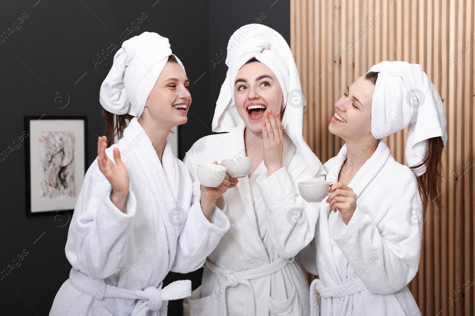 Photo of Happy women with cups of healthy drink in bathrobes after spa procedures indoors