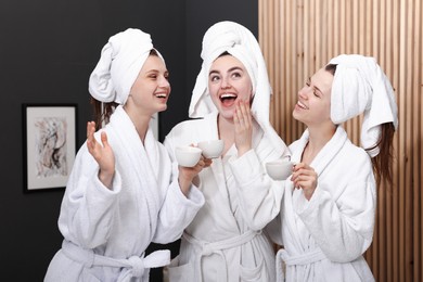 Photo of Happy women with cups of healthy drink in bathrobes after spa procedures indoors