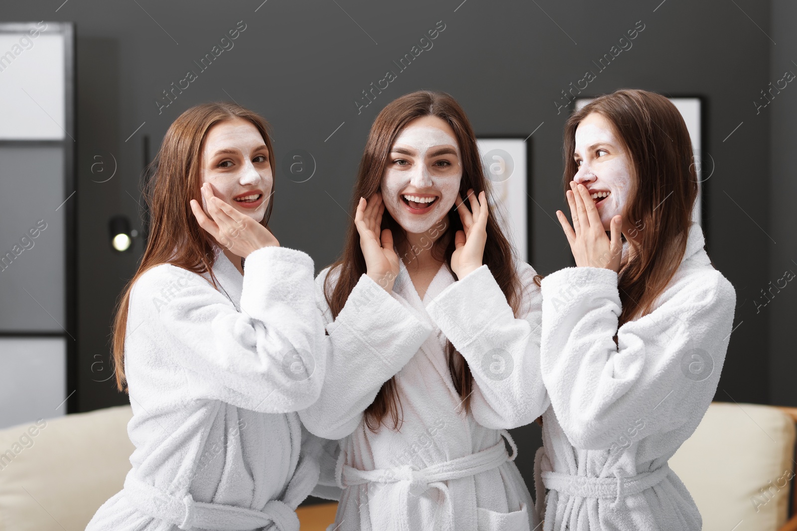 Photo of Happy women with facial masks in bathrobes after spa procedures indoors