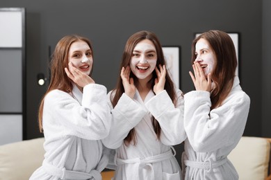 Photo of Happy women with facial masks in bathrobes after spa procedures indoors