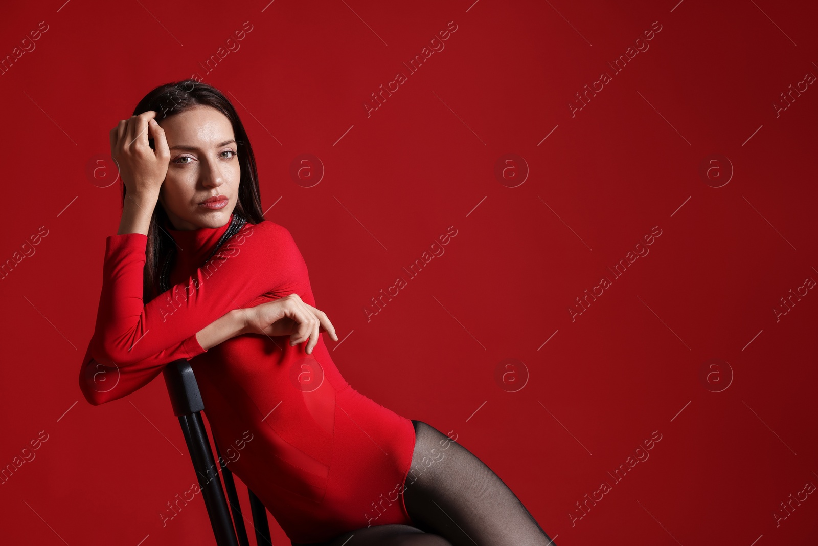 Photo of Beautiful woman in stylish outfit and chair on red background, space for text
