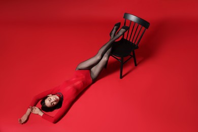 Photo of Portrait of beautiful woman in stylish outfit and chair on red background