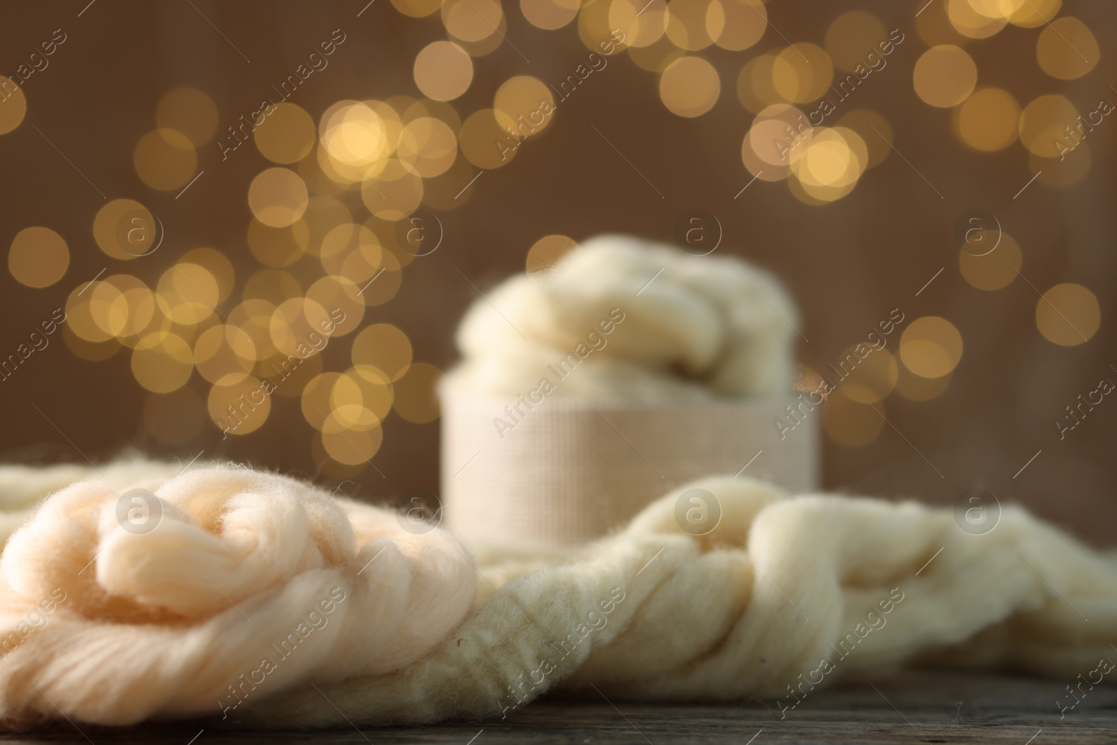 Soft felting wool on wooden table against brown background with blurred lights, closeup Photo of Soft felting wool on wooden table against brown background with blurred lights, closeup