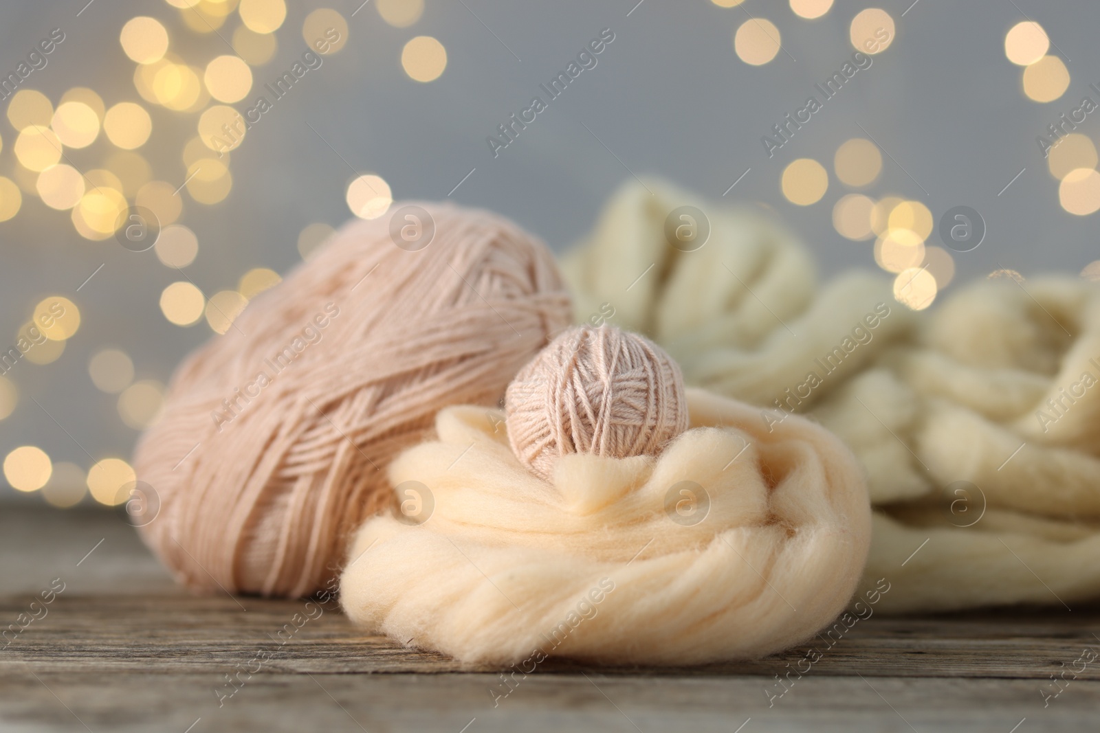Photo of Soft felting wool and yarns on wooden table against grey background with blurred lights, closeup