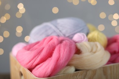Photo of Soft felting wool in crate against grey background with blurred lights, closeup